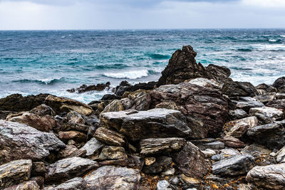 Rocks on shore by sea against sky