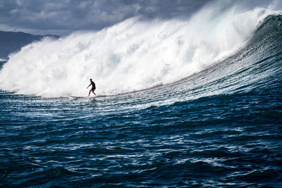 Silhouette man surfing in sea against sky