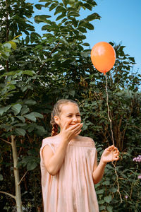 Midsection of girl holding red balloon against trees