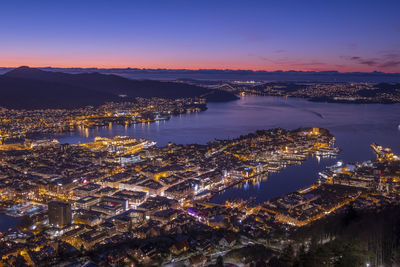 High angle view of illuminated city by buildings against sky at sunset