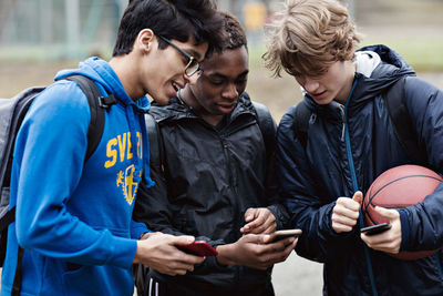 Friends talking while looking at smart phone on playing field