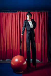 Male performer standing on stilts in front of red curtain