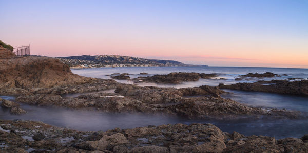 Scenic view of rocky shore against sky during sunset 