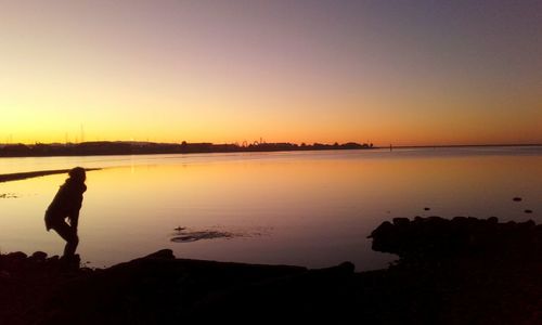 Rear view of silhouette woman standing by sea against sky during sunset