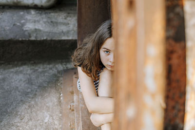 Teenage girl hugging knees while sitting on abandoned window sill