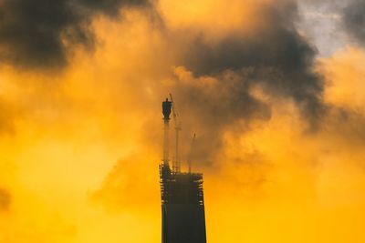 Low angle view of smoke stacks against sky during sunset