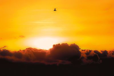 Silhouette airplane flying against orange sky