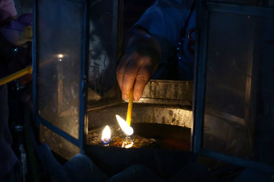 Cropped image of hand lighting candle in lantern