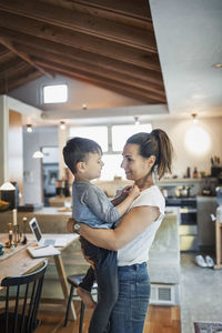 Happy woman carrying son at home