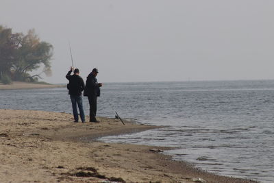 Men fishing on sea shore against clear sky