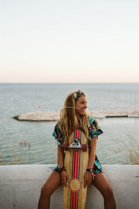 Woman with arms raised against sea against clear sky