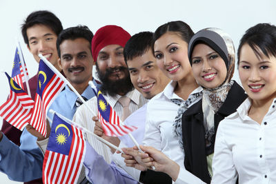 Portrait of smiling colleagues holding malaysia flags against white background