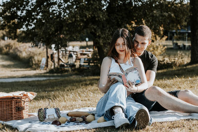 One happy girl sits on a blanket  reads a book while a guy hugs her waist on a summer day close-up