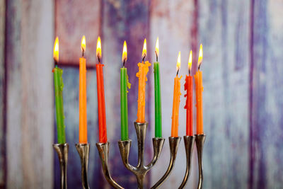 Close-up of multi colored illuminated candles against wooden wall