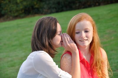 Woman whispering to female friend while sitting outdoors