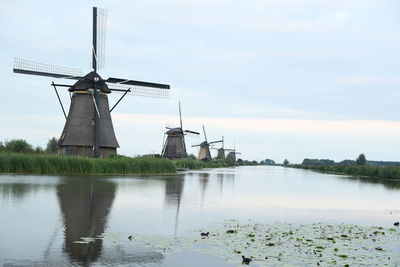 Traditional windmill by lake against sky