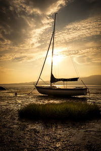 Sailboat moored on sea against sky during sunset