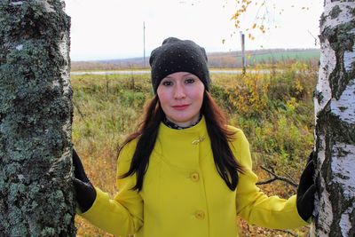 Portrait of smiling young woman standing on tree trunk