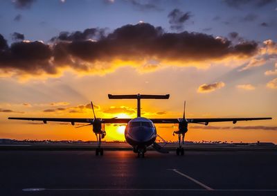 Silhouette airplane on runway against sky during sunset