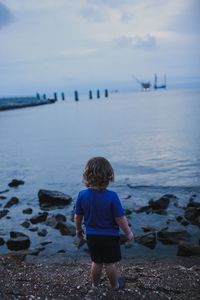 Rear view full length of boy standing on shore at beach