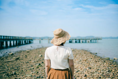 Rear view of woman in hat standing at beach