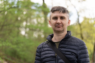 A middle-aged man on a blurred background of early spring greenery looking at camera