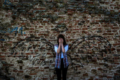 Portrait of young woman standing against brick wall