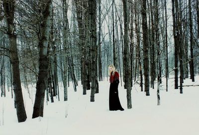 Full length of woman standing on snow covered field in forest