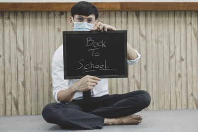 Portrait of man wearing flu mask holding slate against wall