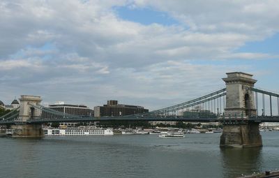 Chain bridge over river against cloudy sky