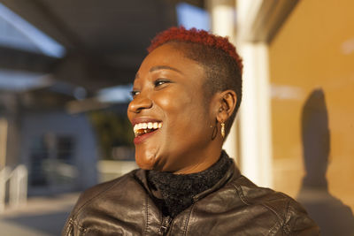 Side view of beautiful afro woman posing near the window and smiling while looking away on a sunny day