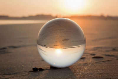 Close-up of crystal ball on beach against sunset sky