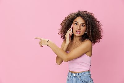 Portrait of smiling young woman standing against pink background