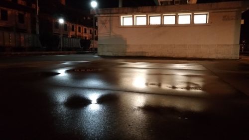 Illuminated wet street by buildings in city at night