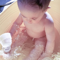 High angle view of naked baby in wading pool on sunny day