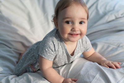 Cute smiling baby girl laying in the bed in morning sun light. grey colors