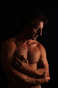 Close-up of shirtless man against black background