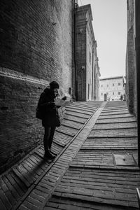 Full length of woman holding paper while standing on walkway amidst buildings