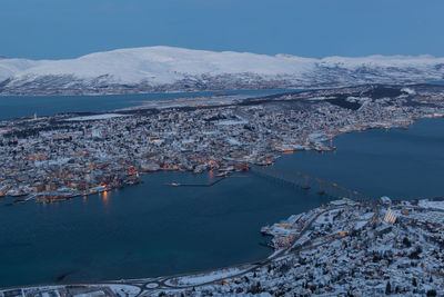 Aerial view of town by fjord with snowcapped mountains against sky
