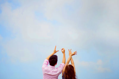 Rear view of man and woman making love sign against sky