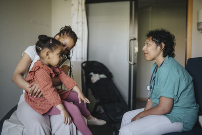 Woman carrying daughter discussing with female doctor in clinic