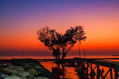 Silhouette tree by sea against orange sky