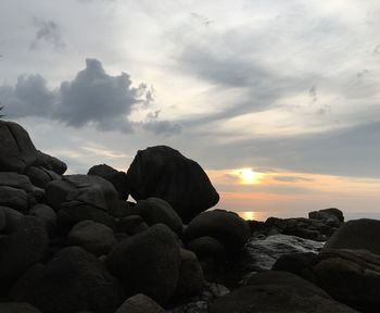 Rocks by sea against sky during sunset