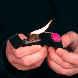 Close-up of hand holding burning candle against black background