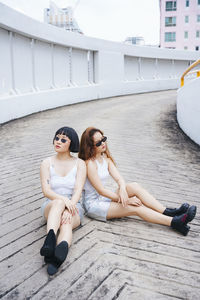 Full length of lesbian couple sitting on footpath outdoors