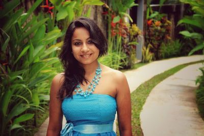 Portrait of beautiful woman standing on footpath by plants