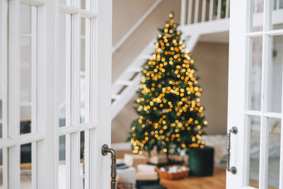 Blurred decorated christmas tree with gift boxes from white door at bright interior at home