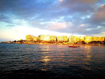 View of city at waterfront against cloudy sky