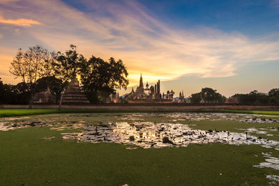 Scenic view of lake by buildings against sky during sunset