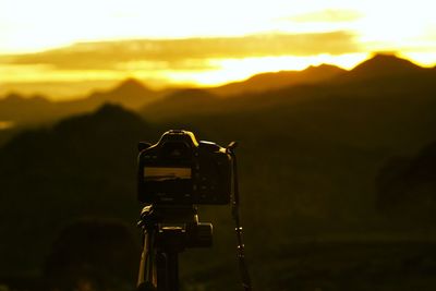 Close-up of camera against mountain during sunset